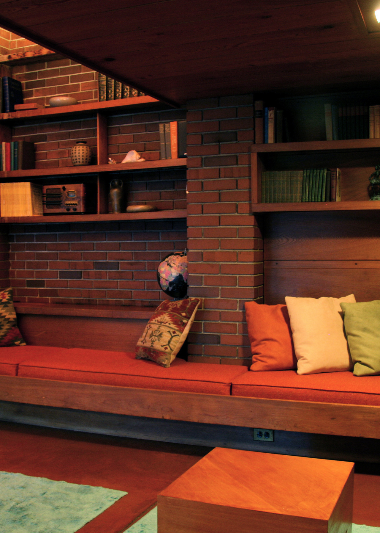 dark, lower ceiling section of a frank lloyd wright house. built in bench seating area with cushions and wooden shelving above