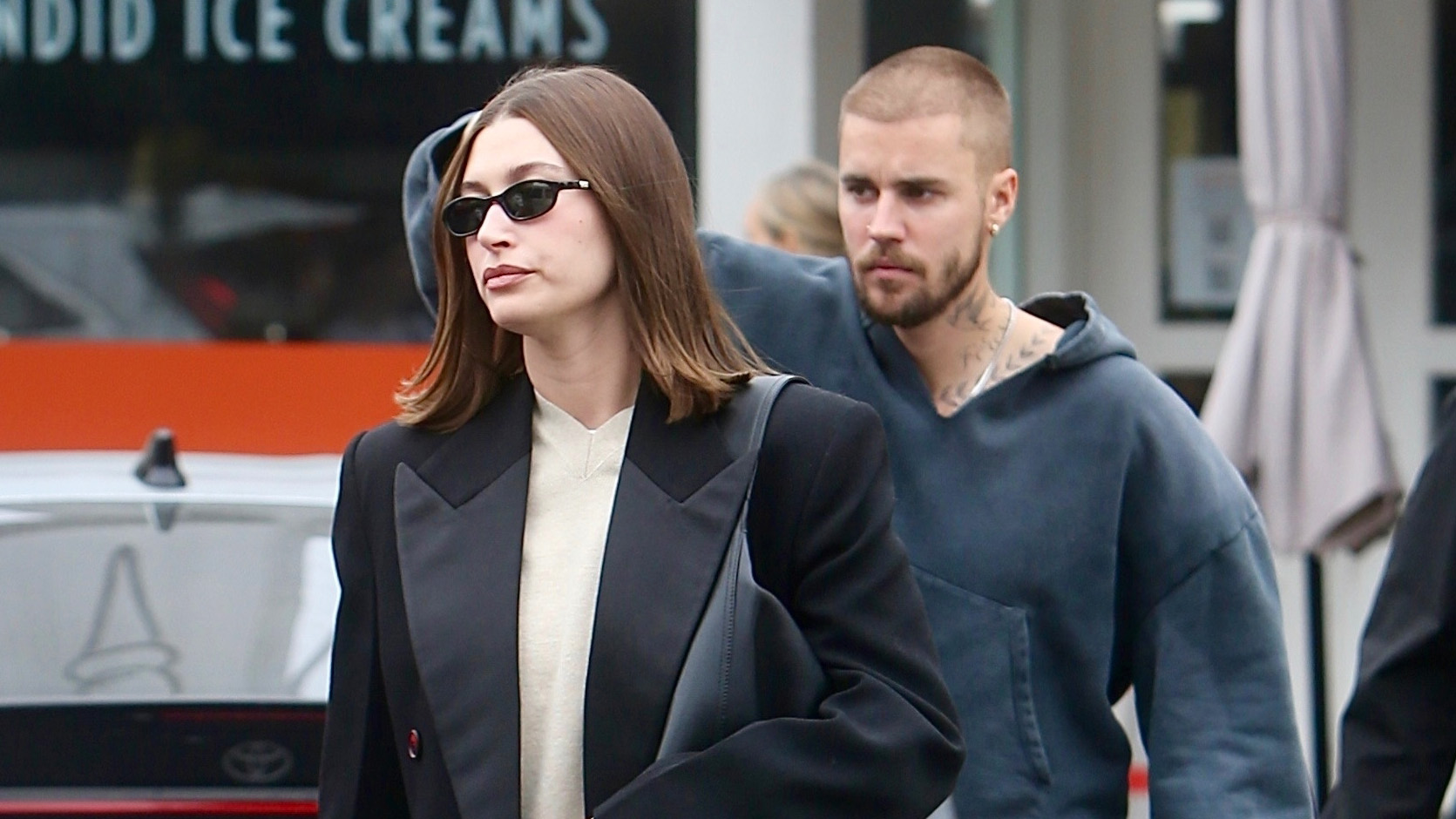 Hailey Bieber wearing a black coat with sweatpants and Ugg Elea slides