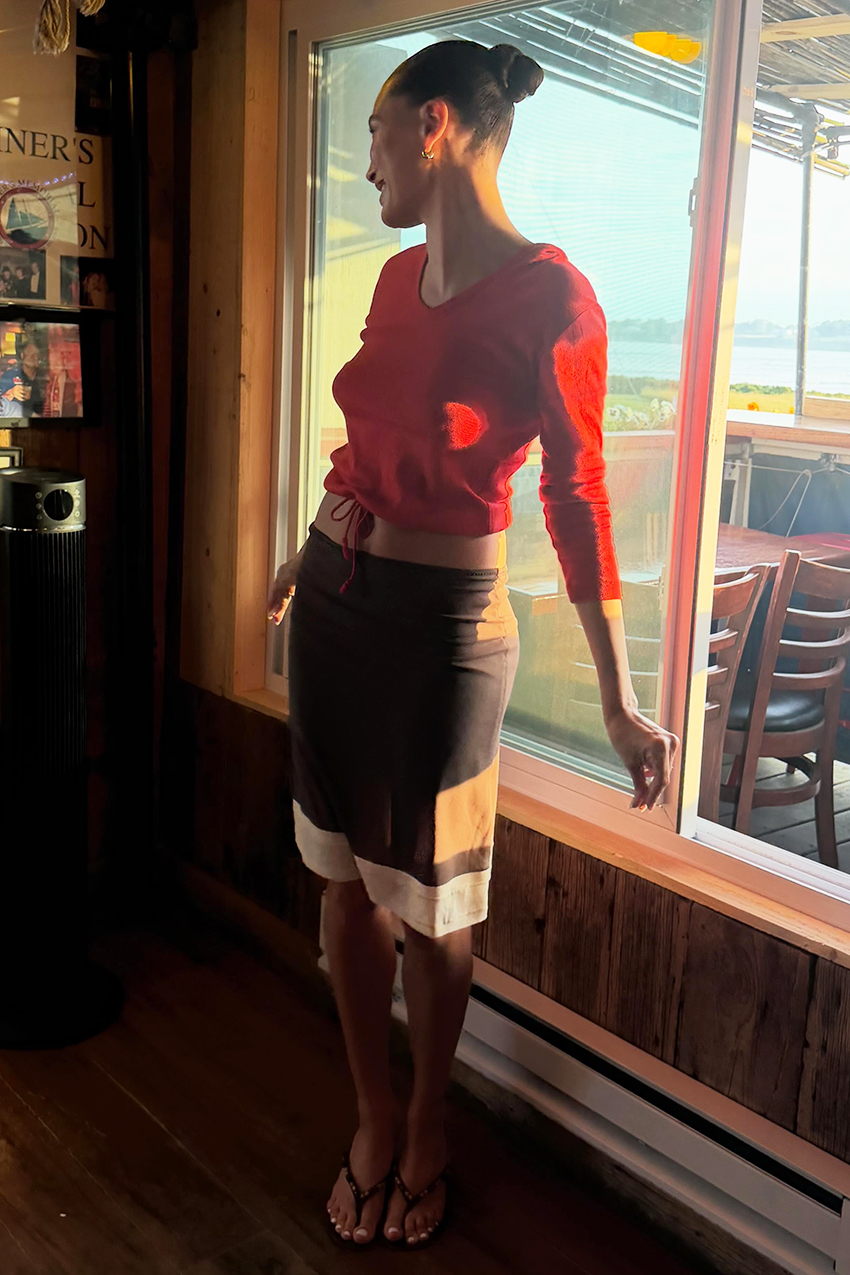 a woman wearing a red longsleeve, brown skirt, and black thong sandals