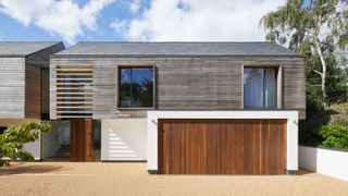 modern house with cantilevered wooden clad first floor, rendered ground floor with garage leading onto resin driveway