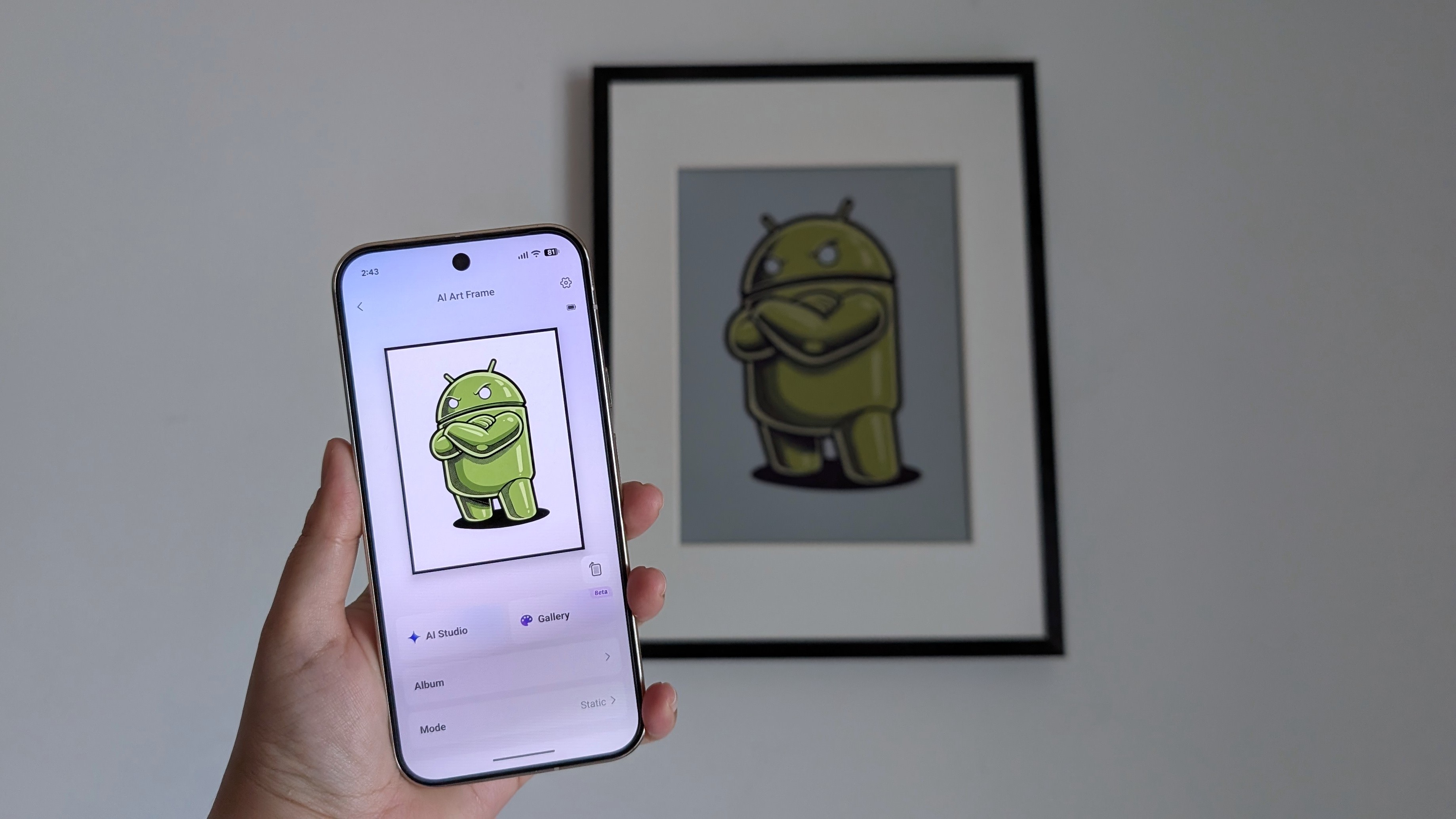 SwitchBot AI Art Frame hung on a plain white wall with a Pixel 10 Pro held up in front of it with the same Android bot artwork