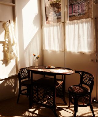 corner of a kitchen with muted pink walls and a bistro set of chairs with cafe style curtains