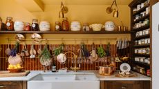 Clodagh McKenna's kitchen with yellow walls, burgundy backsplash tiles, marble countertops, and wooden open shelved displaying collected kitchenware and decor
