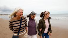 Three senior female friends walking along a beach smiling and relaxed