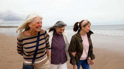 Three senior female friends walking along a beach smiling and relaxed