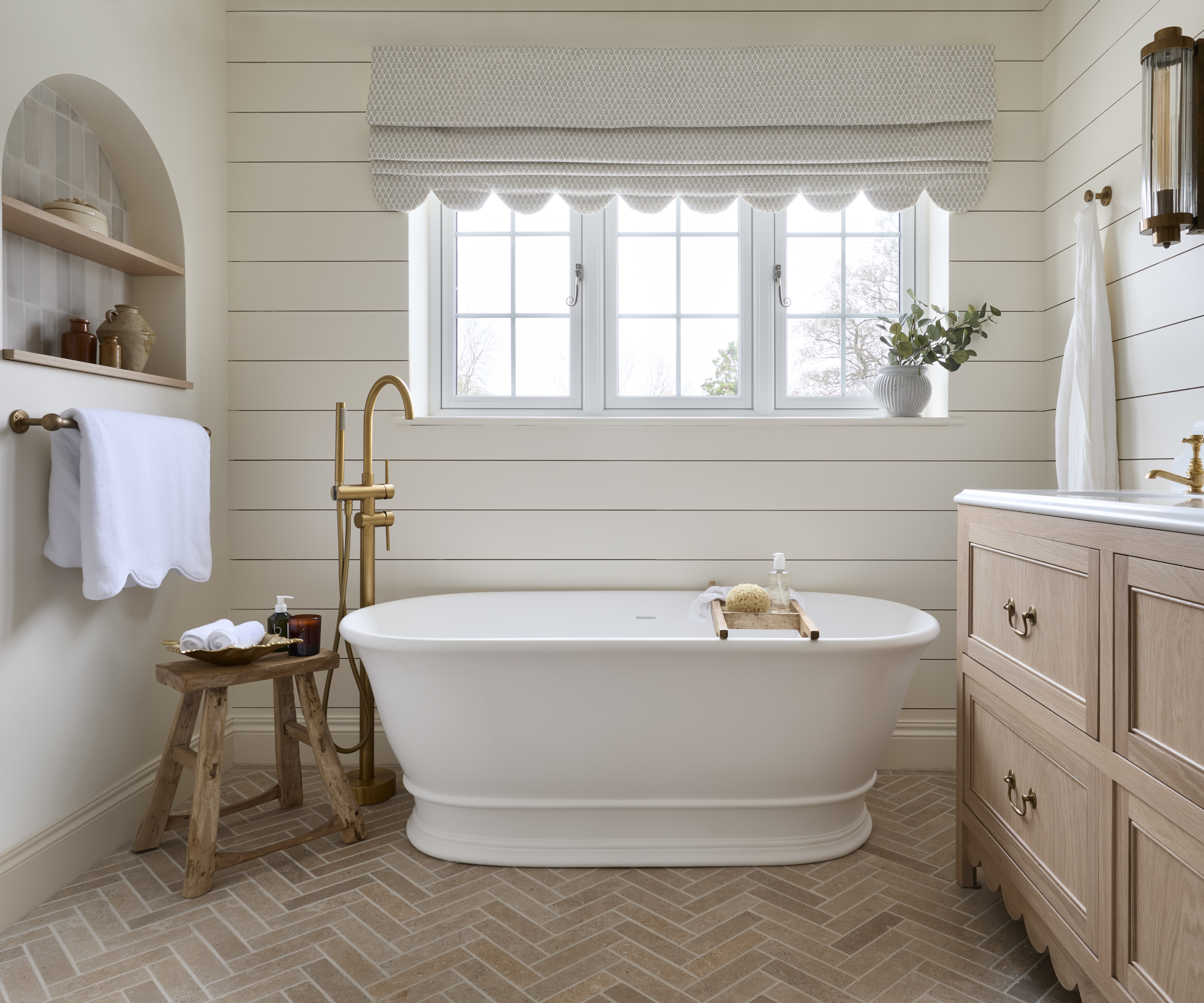 bathroom with white wall panelling, herringbone floor, freestanding bath and wooden vanity