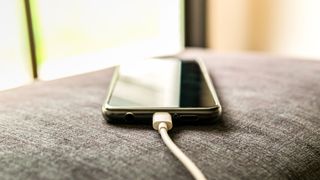 A phone plugged in and charging on the arm of a sofa