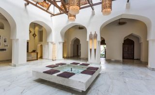 Open courtyard with marble tiles and marble fountain, large arches and copper lanterns
