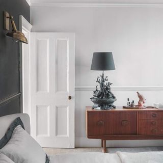 A white bedroom with a charcoal feature wall and a mid-century modern cabinet