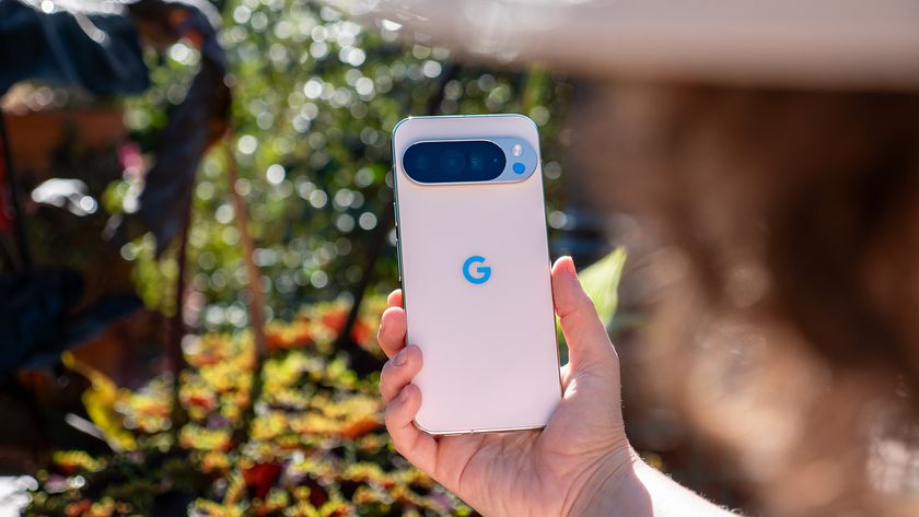 A woman holding up a white Google Pixel 10 Pro XL with colorful plants in the background