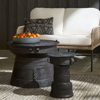 Black outdoor side tables on top of a rustic rug with a white and rattan outdoor sofa behind