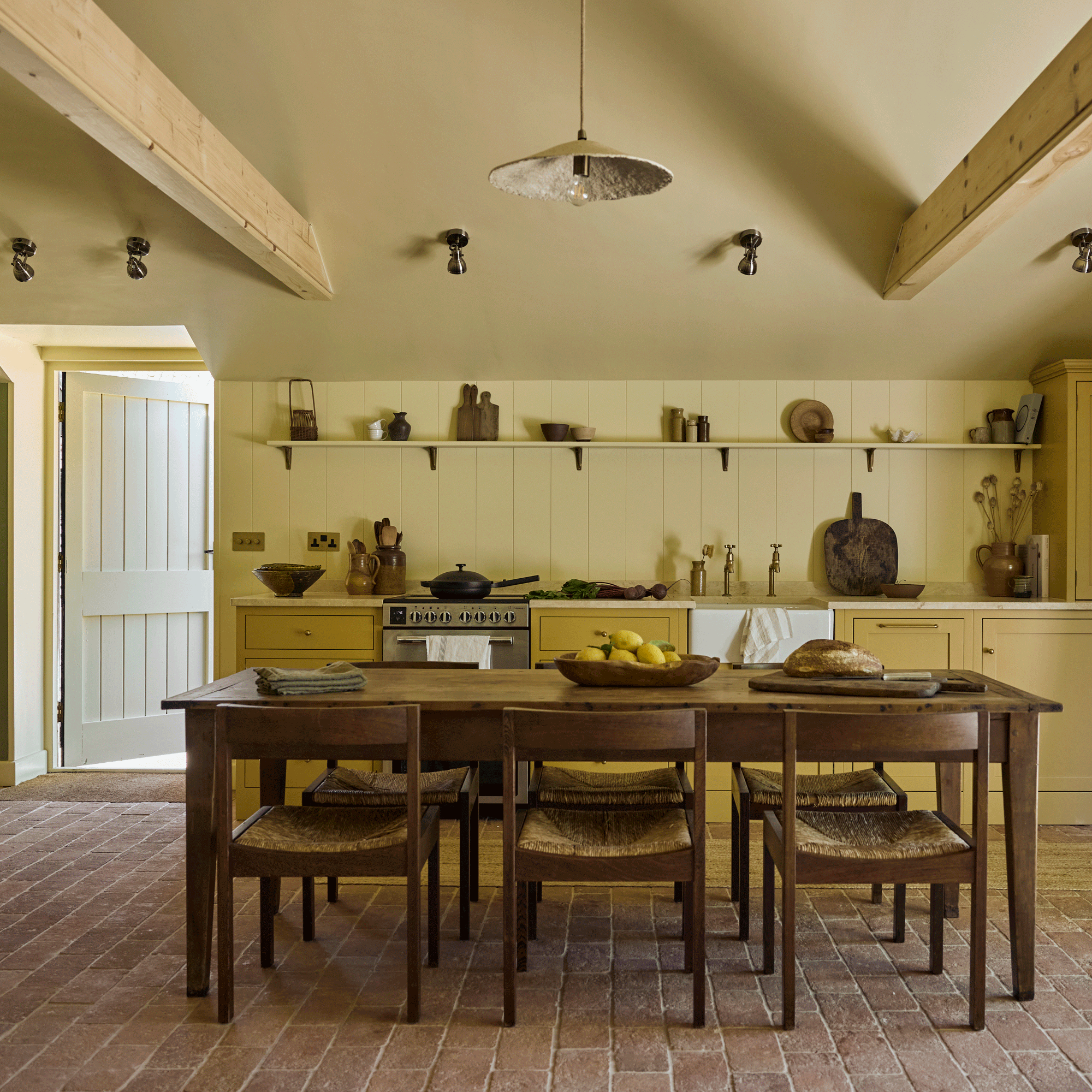 an open plan kitchen diner with yellow cabinetry and walls and an old reclaimed table and chairs