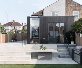 A wraparound kitchen extension with large floor to ceiling glazing broken up with dark exterior timber cladding