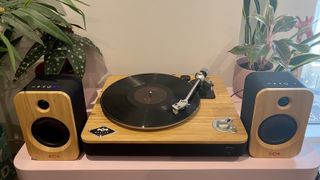 House Of Marley Stir It Up Wireless Turntable on side table with bookshelf speakers and plants