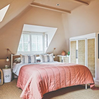 A peach-painted attic bedroom with a tonal bedspread on the bed and downlights at the ceiling