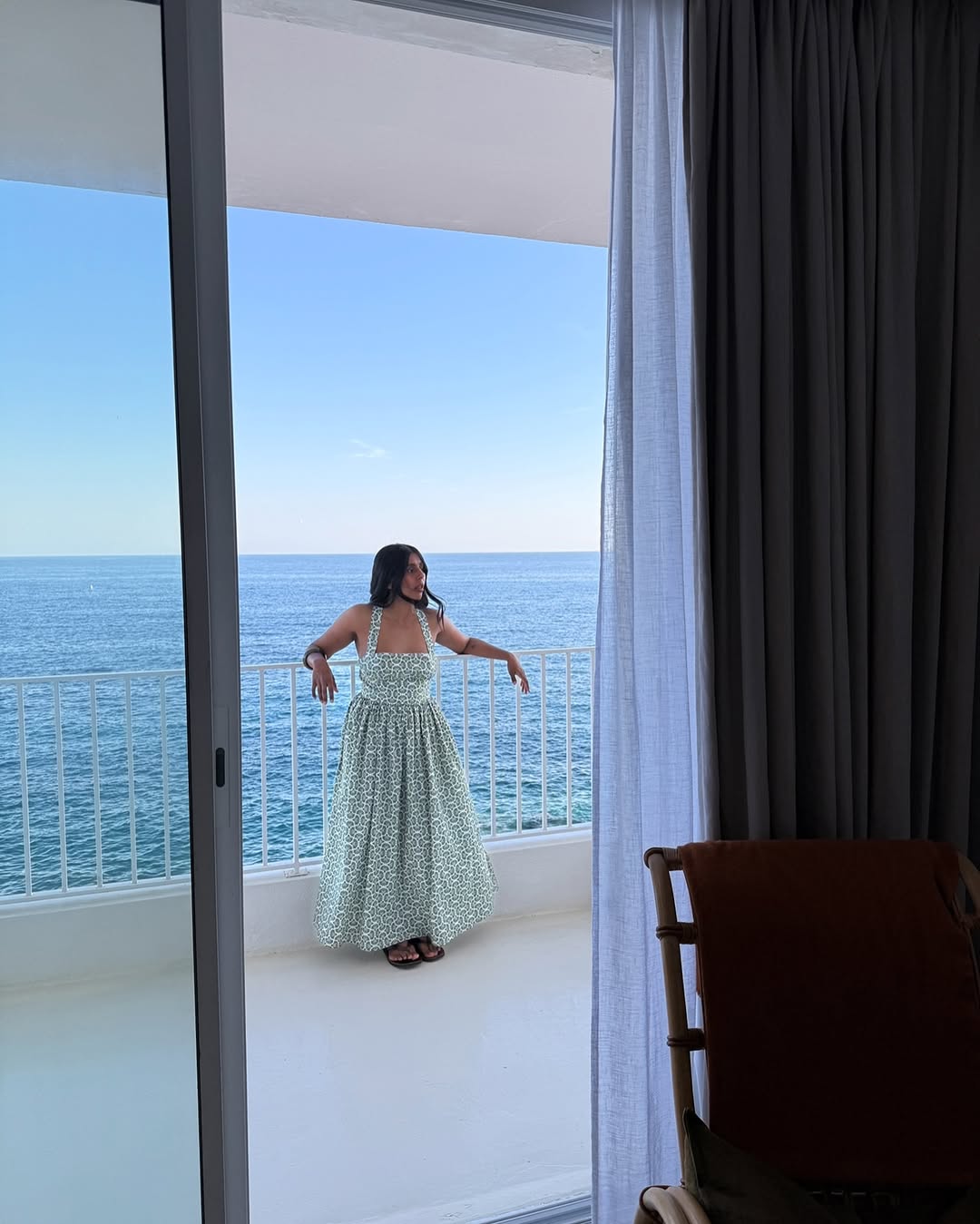 @monikh wears a green printed maxi dress whilst standing on a balcony overlooking the ocean
