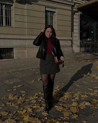 @indiraci wears an elegant winter outfit consisting of a black leather jacket, grey wool miniskirt and a red roll neck knit