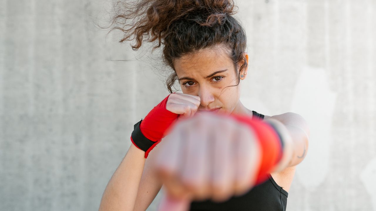 A young woman has her fists up, ready to fight inflation&#039;s impact on her portfolio.