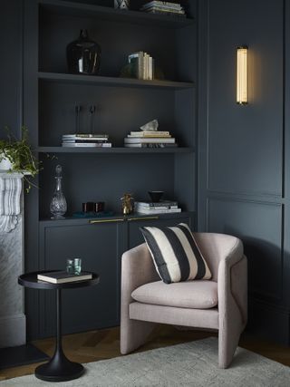 dark living room with armchair in the corner and vertical wall light, bookshelf