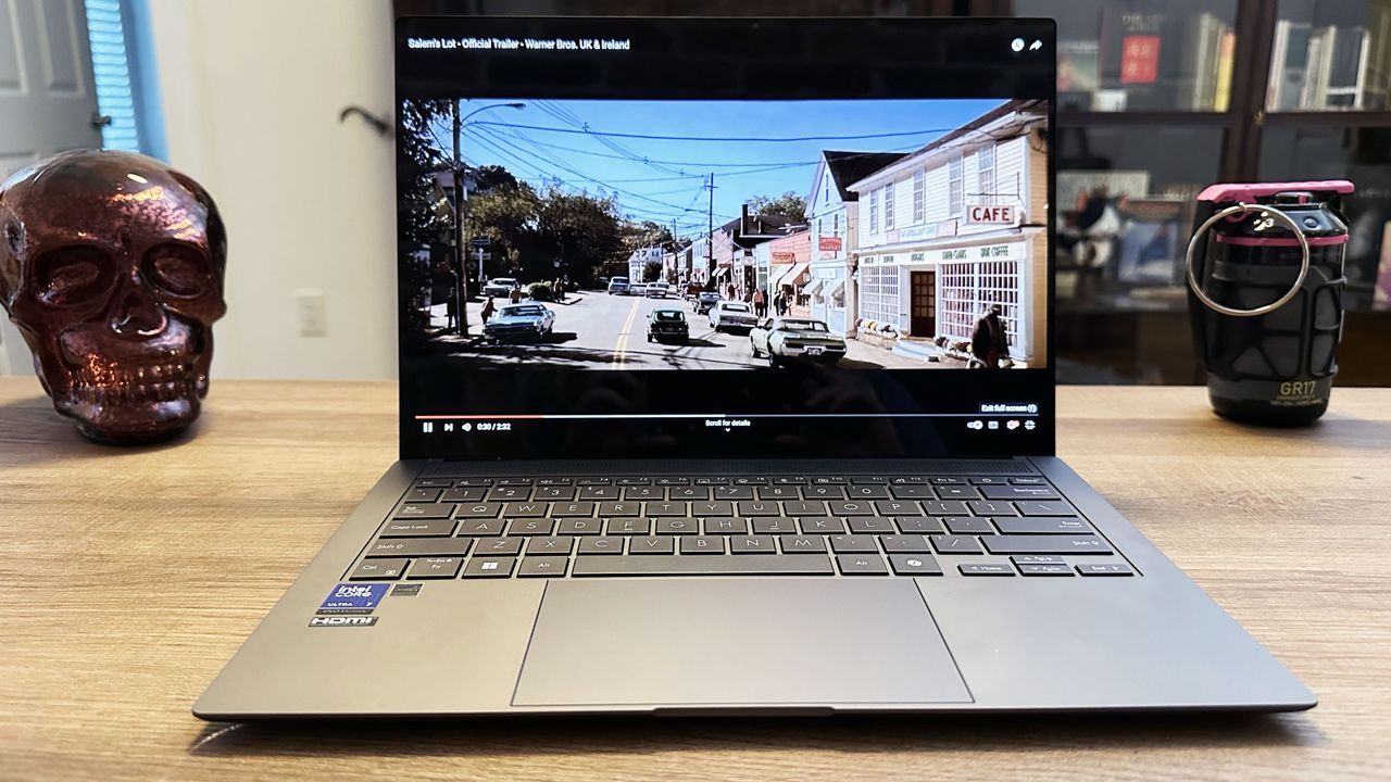 Asus Zenbook S 14 on a wooden desk showing a movie on the display.