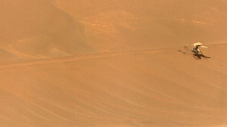 a small dual-rotor helicopter lays dormant on a reddish-orange sand dune