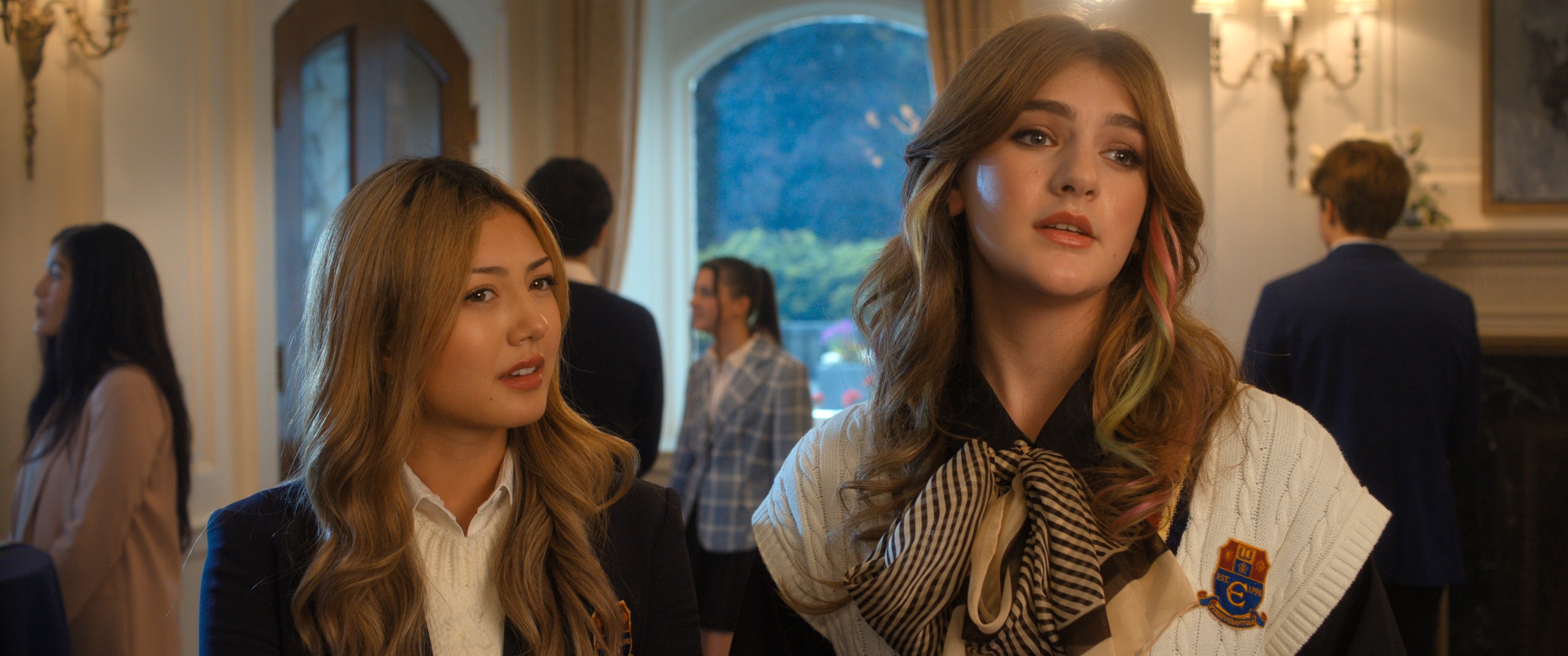 Two female students (Miku Martineau as Teagan Tao and Olga Petsa as Juliet Morny) stand in an ornate den, in Netflix's 'Crew Girl.'