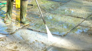 Person in green wellies pressure washing patio slabs