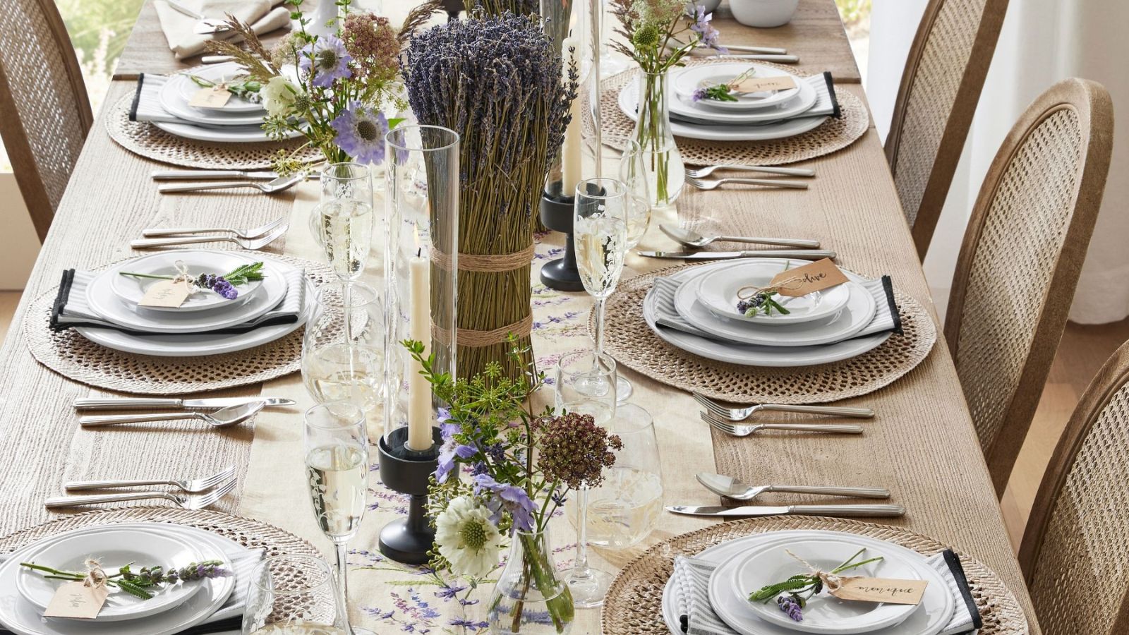 Wooden dining table with white crockery, rattan placemats, large bunches of lavender, and glass bud vases
