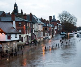 River in flood breaks its banks, covers the road and pavement, and floods the basement of the local pub