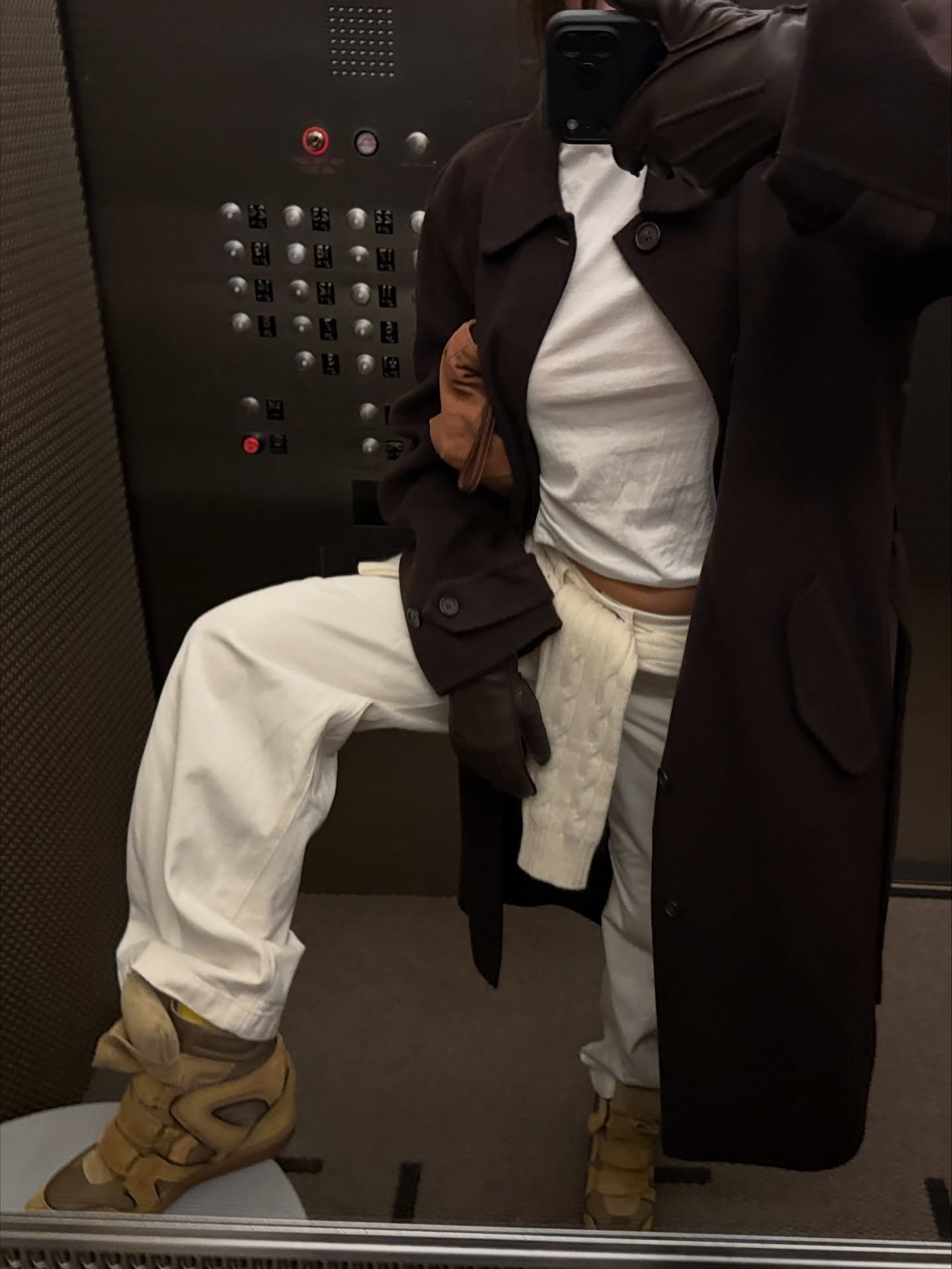 Fashion person izzipoopi wears a trending trainer brand 2026. She wears the Isabel Marant Beckett Wedge trainers. She wears them with white denim jeans, a white tee and brown funnel-neck coat. This image was recently taken from her Instagram.