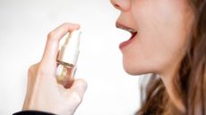 photo of young woman holding up a mouth spray in preparation to spritz it into her mouth
