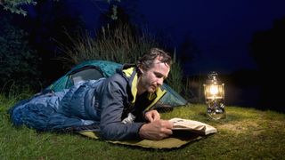 Man in sleeping bag reading by lantern light