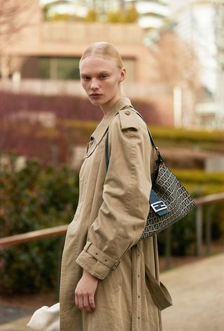 a street-style photo of a woman wearing one of the most popular vintage bags, Fendi baguette with a trench coat