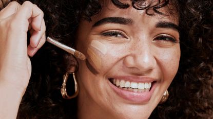 tarte concealer - smiling woman with three different shades of concealer on her cheek - gettyimages 1442518256