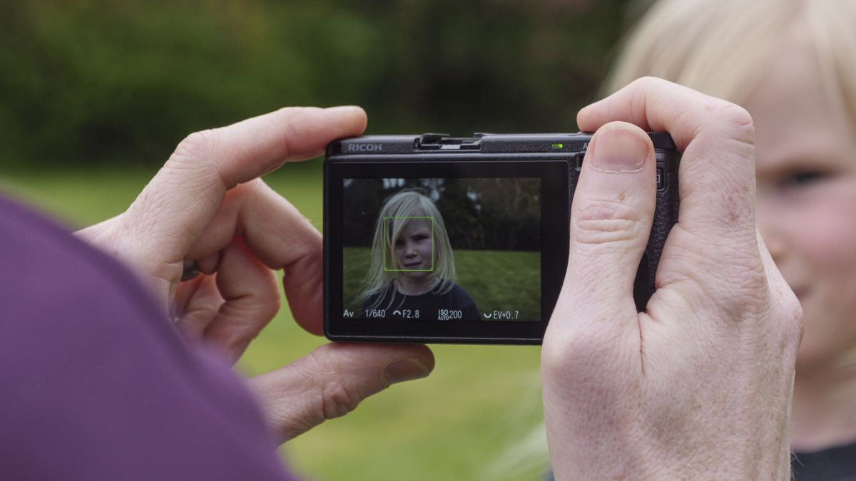 A hand holding the Ricoh GR IIIx camera