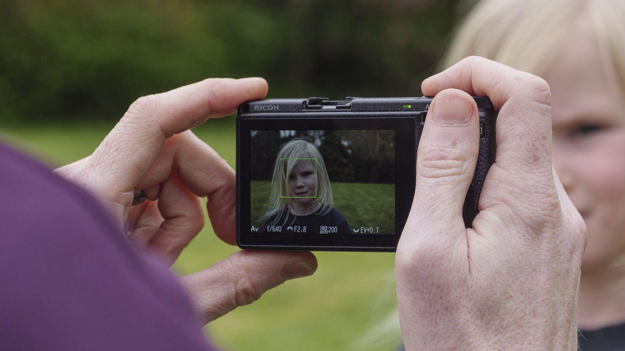 A hand holding the Ricoh GR IIIx camera