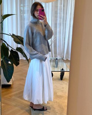 woman taking mirror selfie with gray turtleneck sweater, white skirt, and mule kitten-heel sandals