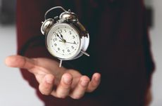 A hand holding an old-fashioned alarm clock