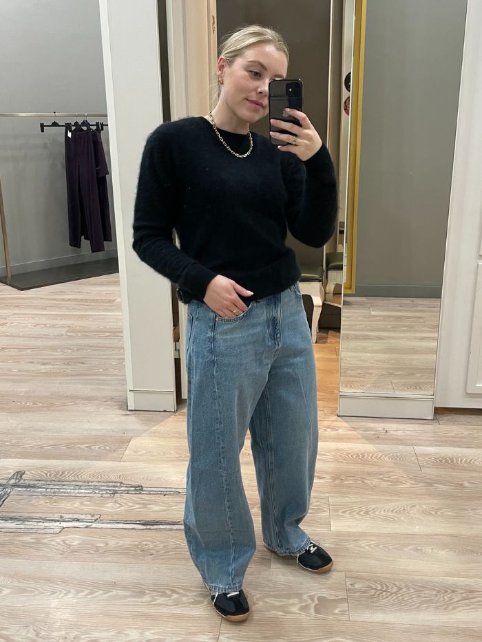 Woman wears black jumper, blue jeans and black trainers