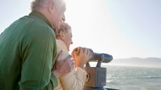 Smiling senior couple looking at ocean with coin-operated binoculars
