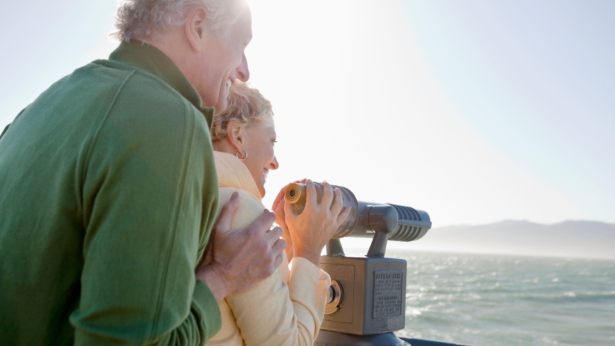 Smiling senior couple looking at ocean with coin-operated binoculars