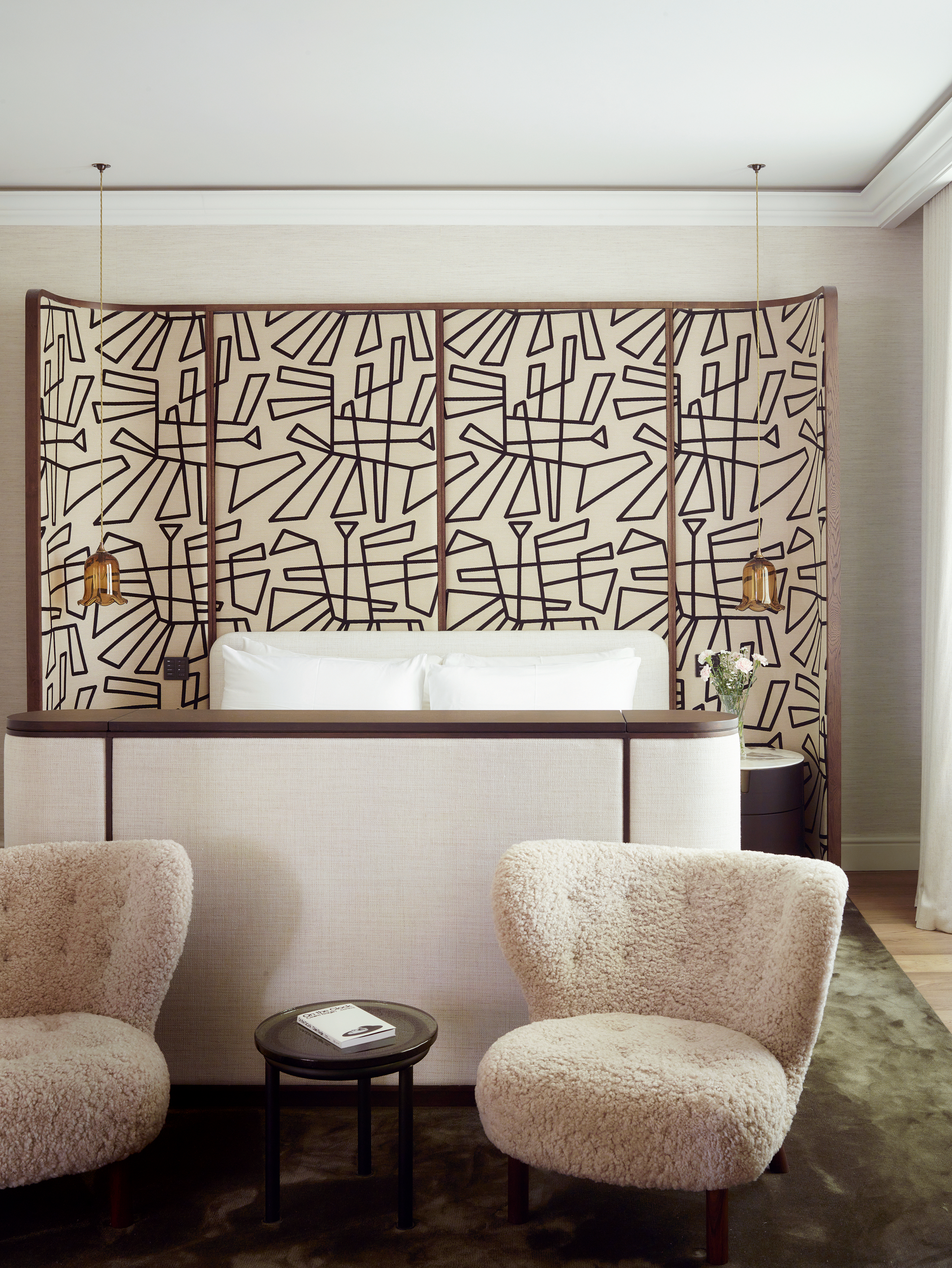 Bedroom with oversized headboard in abstract pattern and two cream boucle armchairs