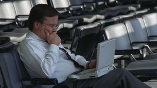 A businessman waiting at the US Air terminal in La Guardia Airport works on his laptop computer.