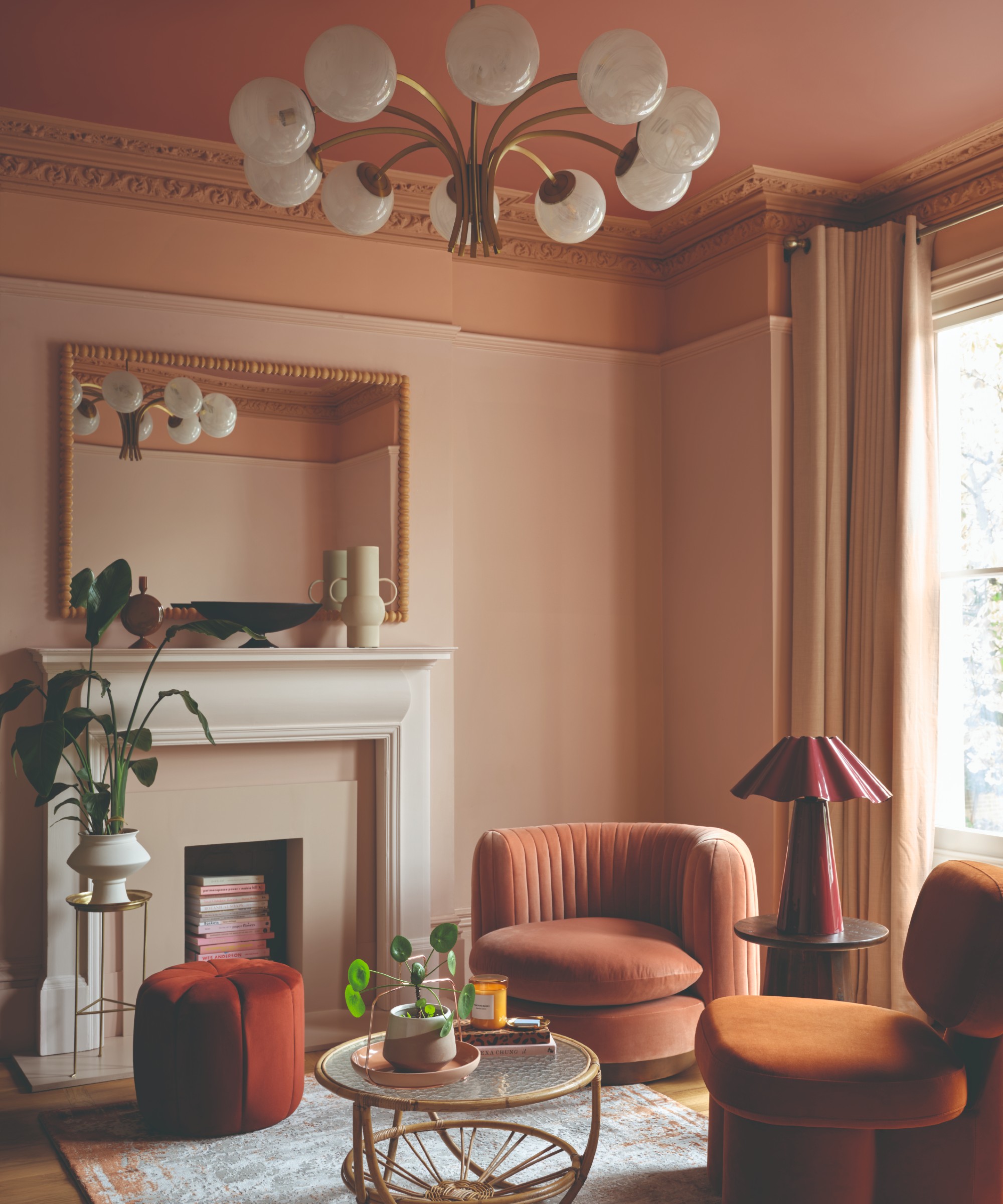 A living room painted in a soft pink on the walls with the picture rail and cornicing painted in a peachy shade and the ceiling covered in a darker pink colour