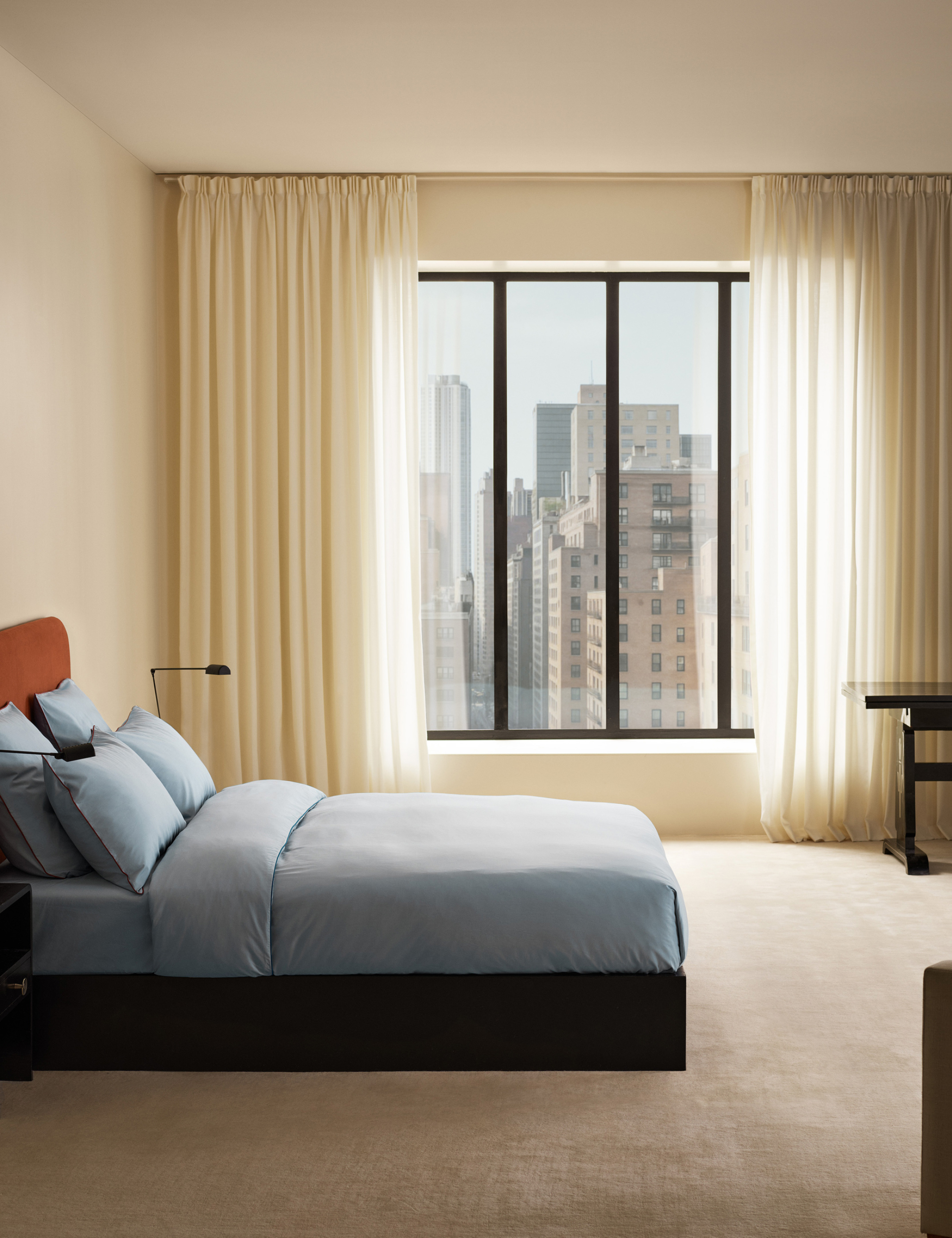 Minimalist NYC bedroom styled with a cream-colored wool rug, matching sheet curtains, and an 'ice blue' bedding set by Nordic Knots