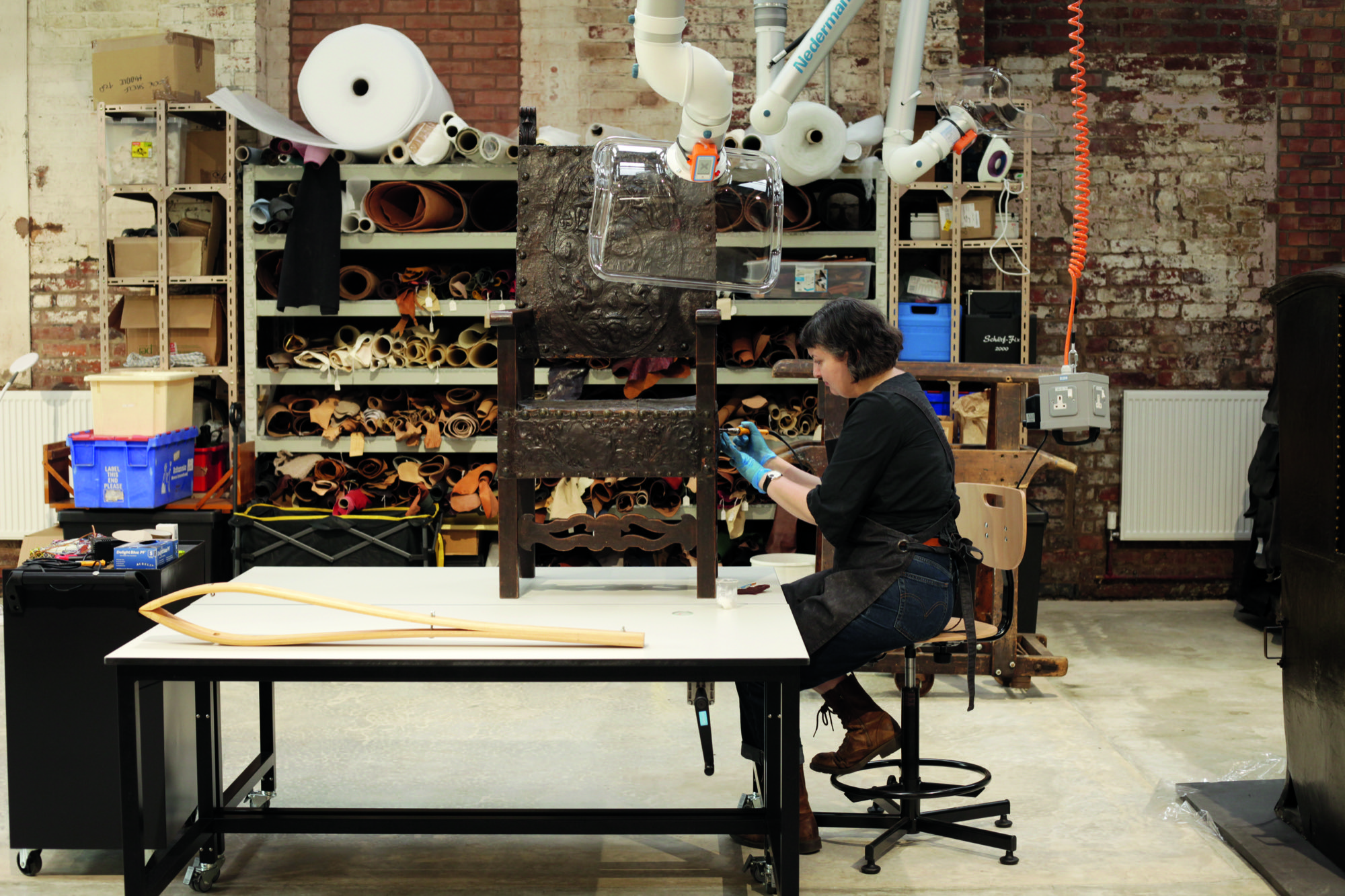 A craftsperson treats a leather bishops chair on a table
