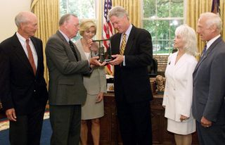 President Bill Clinton (center) is presented a moon rock by Apollo 11 astronaut Neil Armstrong and his wife, Carol Armstrong, alongside Apollo 11 crewmates Michael Collins (far left) and Buzz Aldrin (right) and wife Lois Aldrin, in the Oval Office on July 20, 1999.