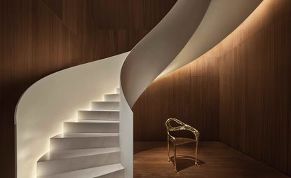 Interior view at The Barcelona Edition hotel, Spain featuring brown wooden walls and floor, a white marble and wood spiral staircase and a gold coloured chair
