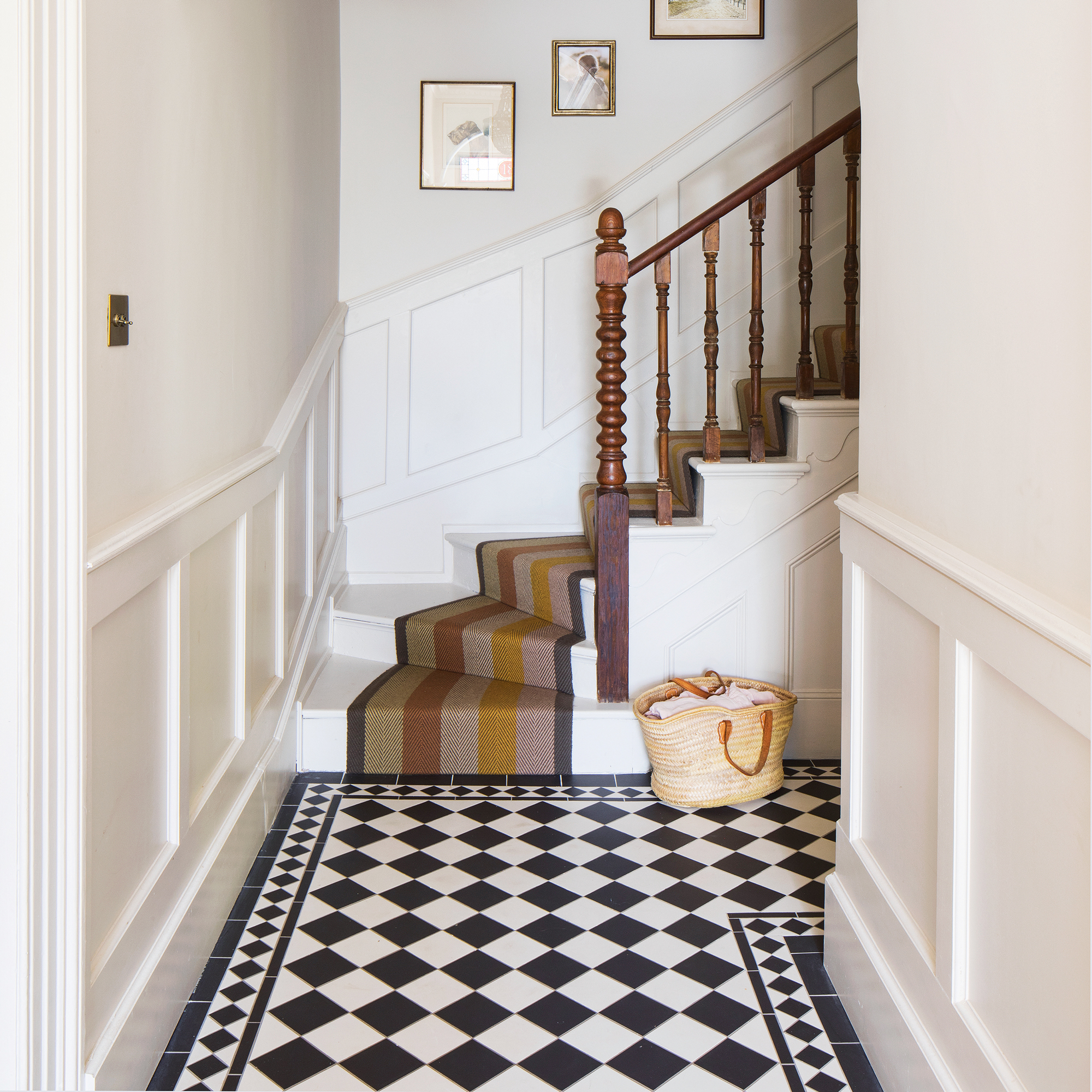 a classic monochrome tiled hallway leading to a flight of stairs with a stair runner