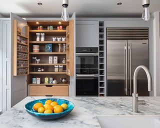A modern grey kitchen with marble island, built-in fridge and oven appliances and pantry